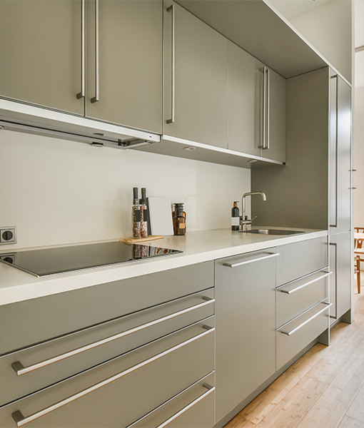 Modern kitchen with sleek, handleless cabinetry in a neutral tone, likely grey or beige, and a white countertop with an integrated hob and sink